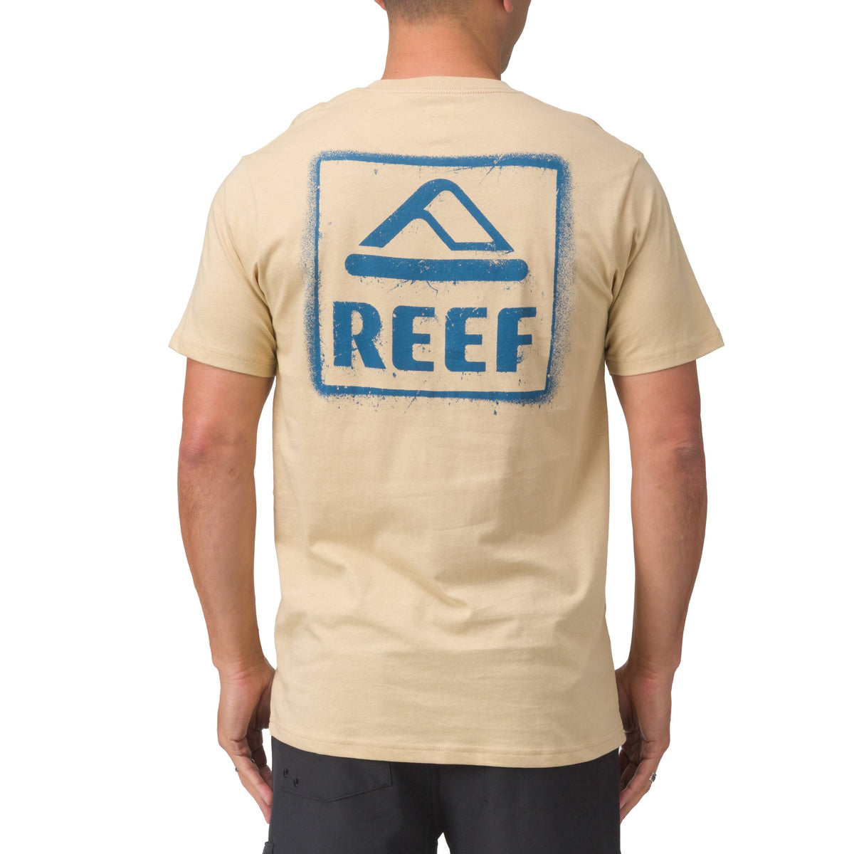 Man wearing beige Xavier Tee showing back with blue REEF logo, surf-inspired comfort apparel for men.