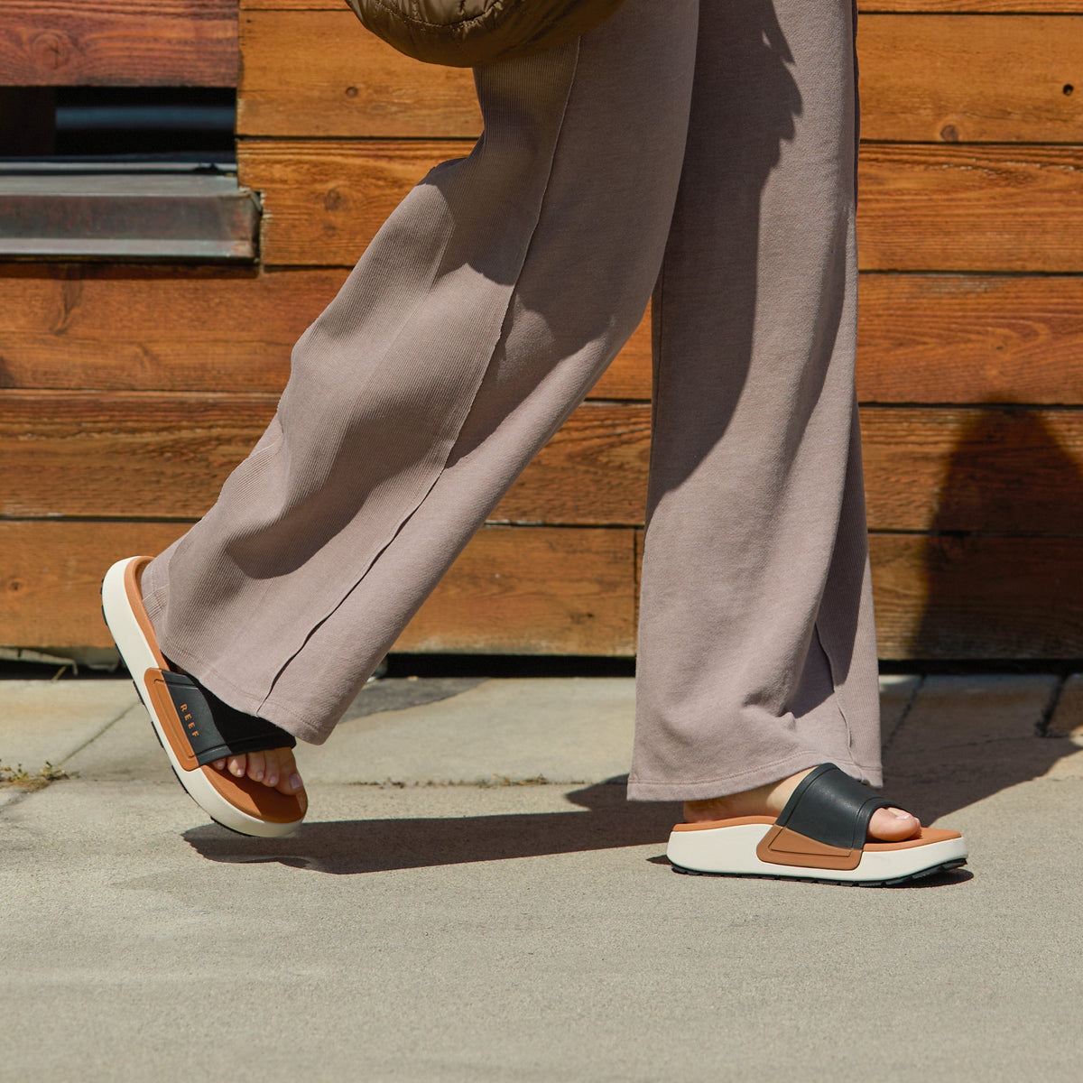 woman wearing Sydnee Cutback Low Black-Tan slide with long pants and walking down the sidewalk