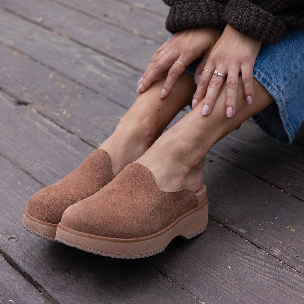 Vista Skye women's walnut suede slip-on shoes facing left showing front and side close-up on wooden deck